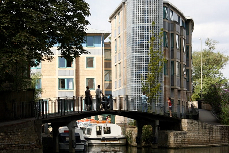 A building with a glass tower is in the background. In the foreground is a bridge across a river.