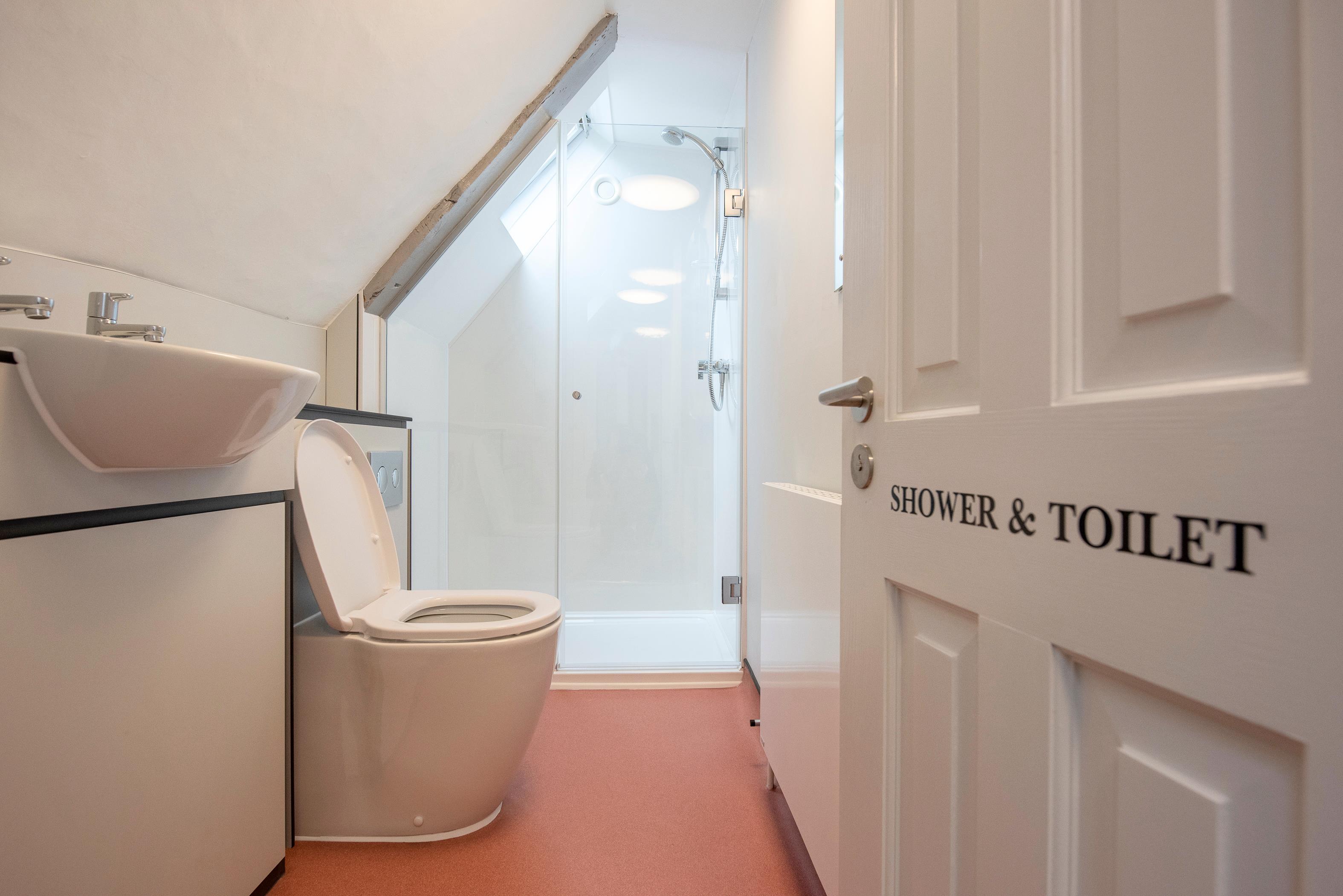 An open door with the words 'shower and toilet' painted on it. Through the door there is a sink, toilet and shower.