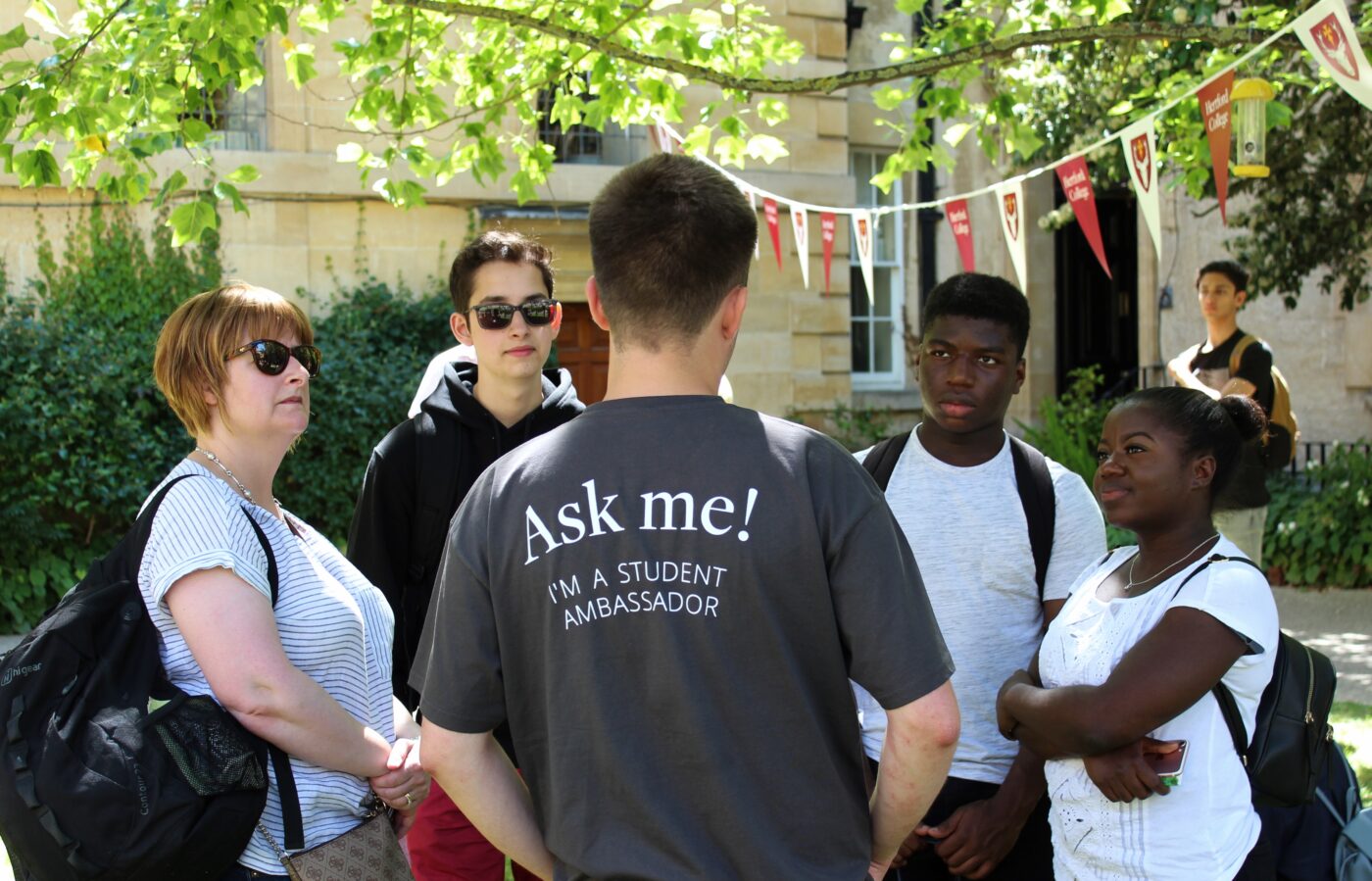 Person in grey student ambassador t-shirt talks to a group of prospective students