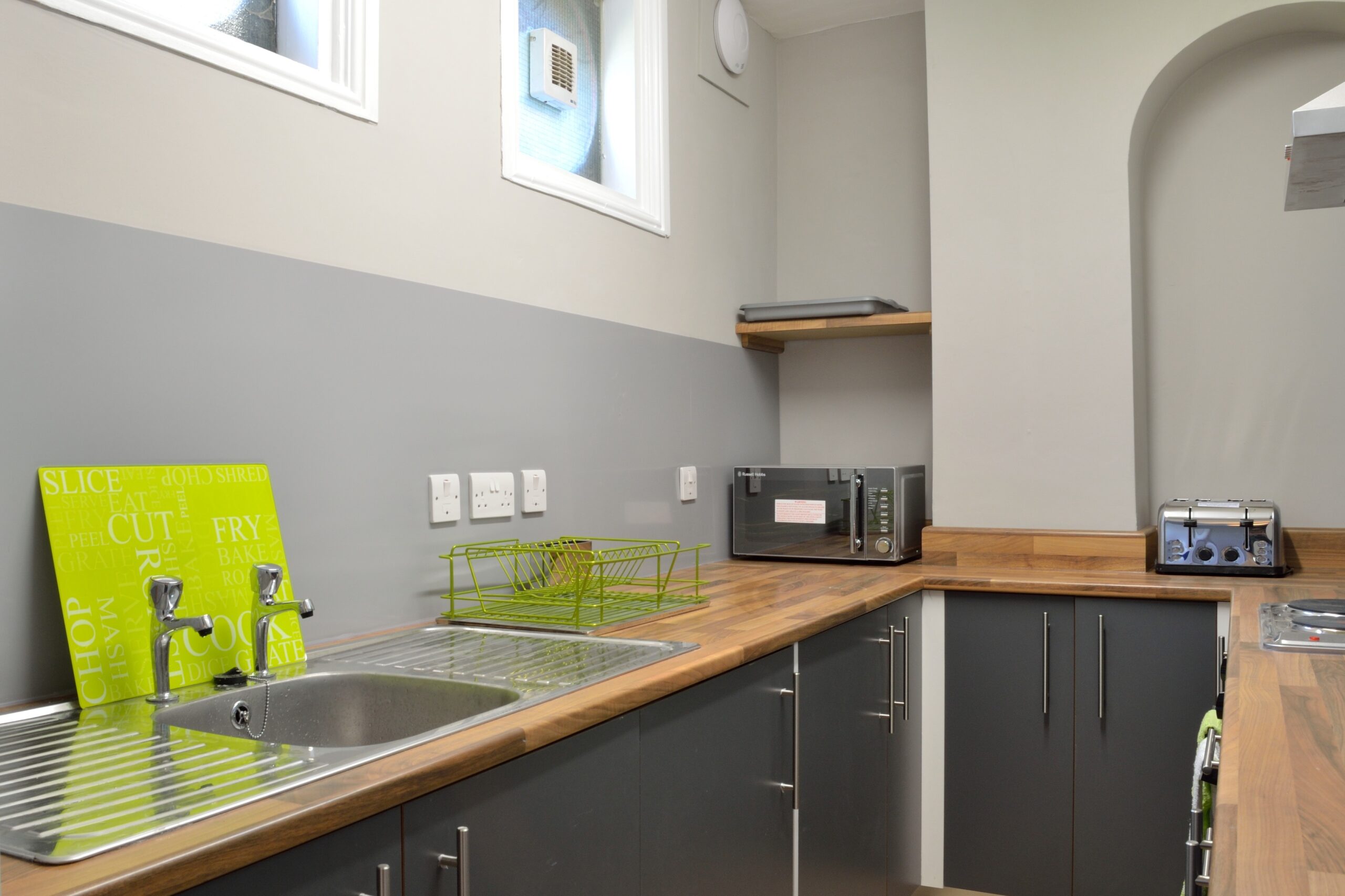 Kitchen with grey units, wooden worktops, sink, microwave and toaster