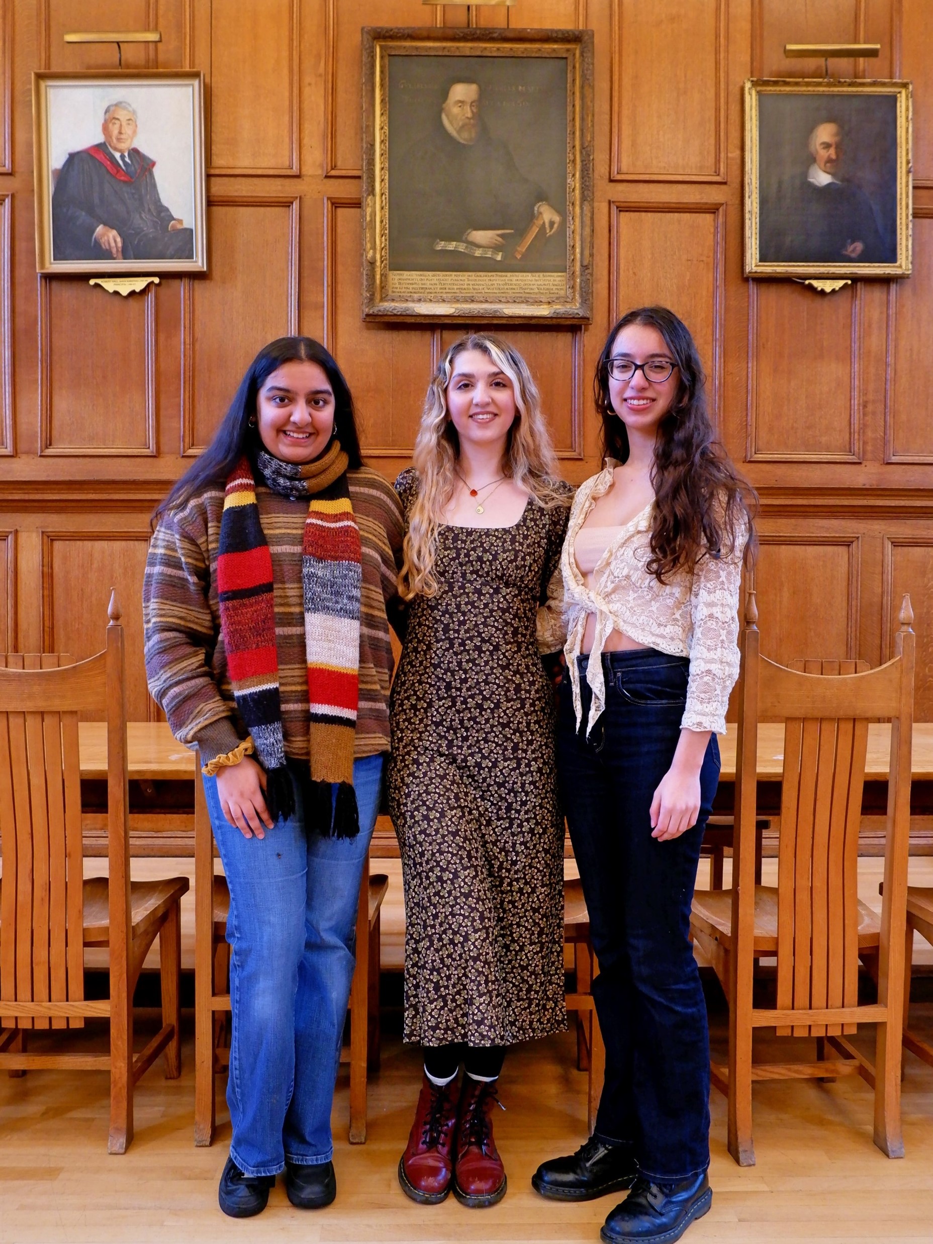 Three women stood in front of three oil paintings of men