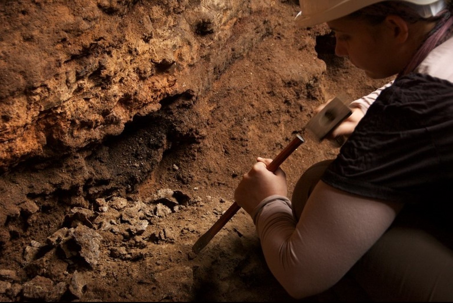 An archaeologist hits a chisel with a hammer in a cave